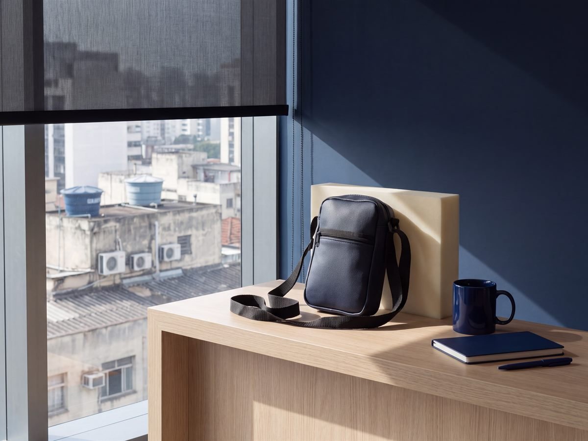Bolsa de ombro 15387A em couro sintético navy, com alça de fita ajustável, apoiada no balcão da recepção de um escritório na Faria Lima, São Paulo